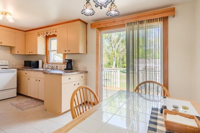kitchen with white electric range, a sink, stainless steel microwave, light tile patterned flooring, and hanging light fixtures