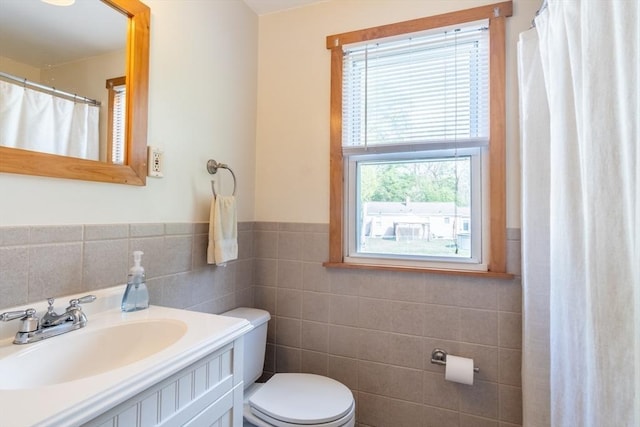 bathroom with tile walls, toilet, a wainscoted wall, and vanity