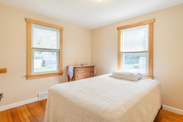 bedroom with multiple windows, wood finished floors, and baseboards