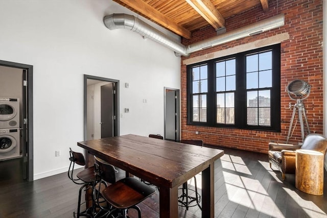 dining area with stacked washer / drying machine, dark wood finished floors, a towering ceiling, and brick wall