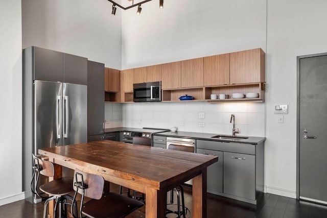 kitchen featuring dark countertops, a high ceiling, stainless steel appliances, open shelves, and a sink