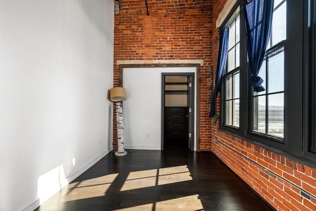 spare room with brick wall, hardwood / wood-style floors, and baseboards