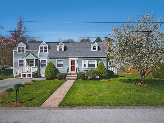 cape cod house with a chimney, a shingled roof, and a front lawn