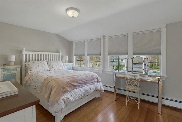 bedroom with vaulted ceiling, baseboard heating, and wood finished floors