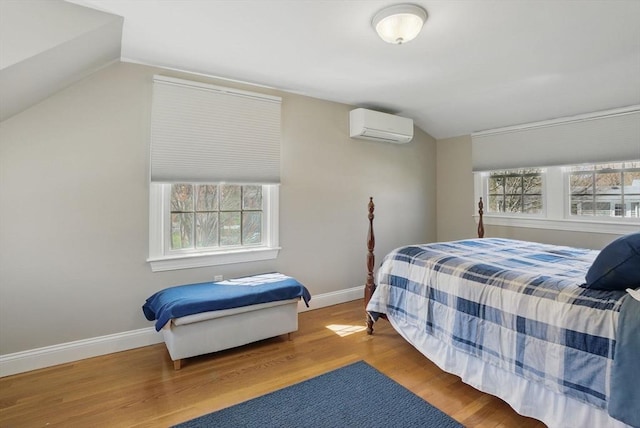 bedroom with baseboards, vaulted ceiling, wood finished floors, and a wall mounted air conditioner