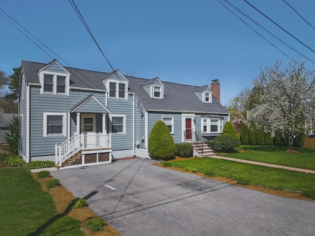 cape cod house with a shingled roof, a front yard, and a chimney