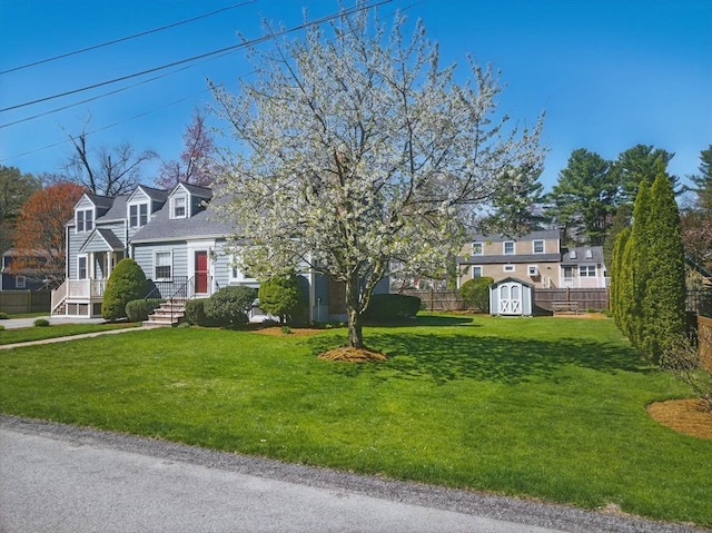 new england style home featuring a storage unit, an outdoor structure, fence, and a front yard