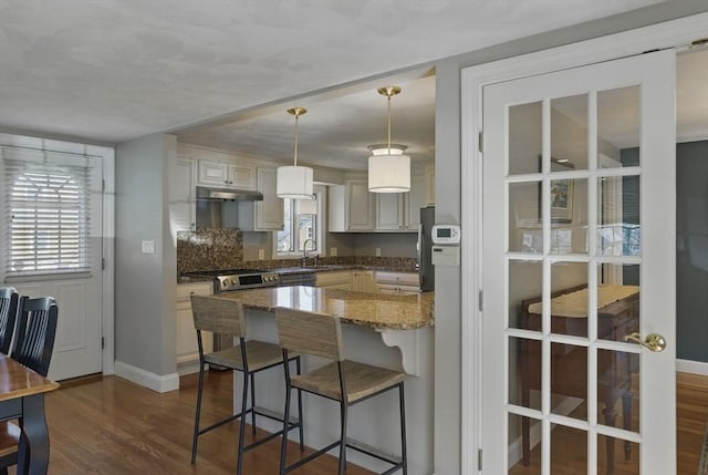 kitchen featuring baseboards, stone countertops, a breakfast bar area, dark wood-style floors, and under cabinet range hood