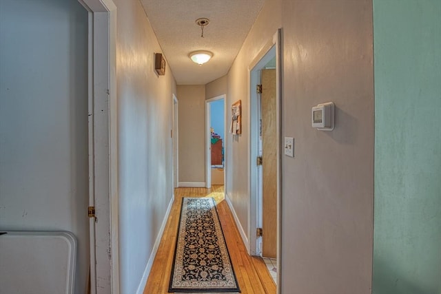 hallway with a textured ceiling and light hardwood / wood-style floors