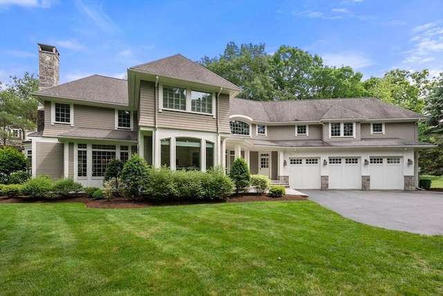 view of front of property featuring a chimney, driveway, a garage, a front lawn, and a shingled roof