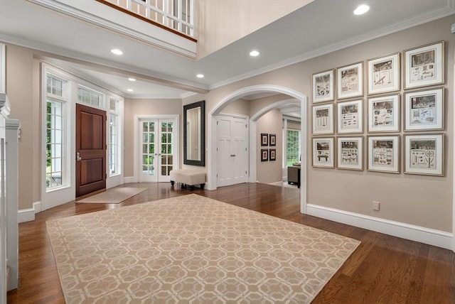 entrance foyer featuring arched walkways, dark wood-style flooring, baseboards, crown molding, and recessed lighting