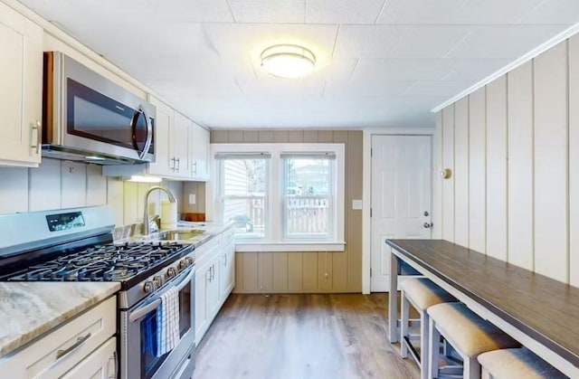 kitchen with stainless steel appliances, sink, white cabinets, light stone counters, and light hardwood / wood-style floors