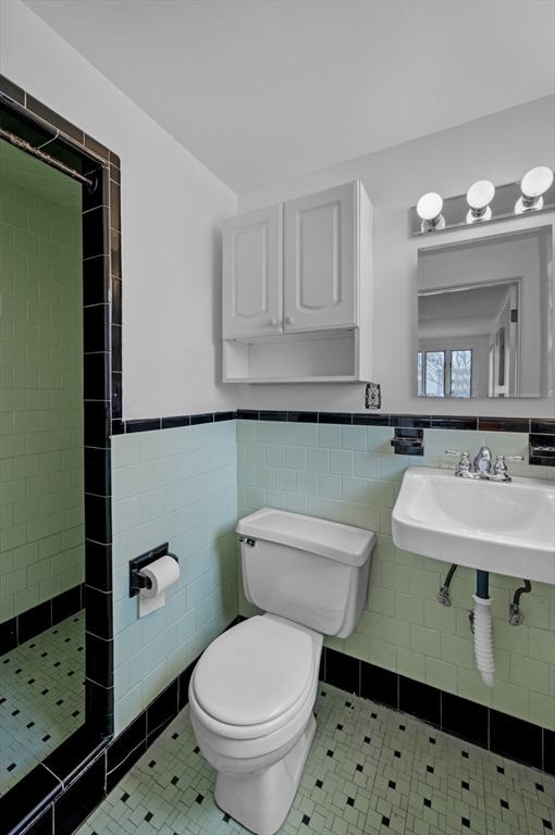 bathroom featuring a sink, a wainscoted wall, tiled shower, and toilet