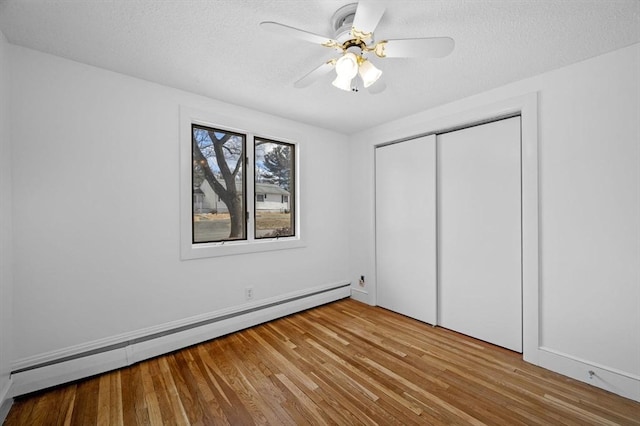 unfurnished bedroom featuring a closet, a textured ceiling, a baseboard heating unit, and wood finished floors