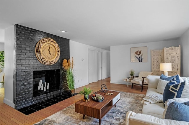 living area with baseboards, a brick fireplace, and wood finished floors