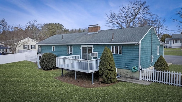 back of house featuring fence, roof with shingles, a chimney, a deck, and a lawn