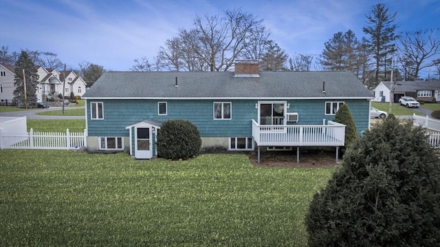 rear view of property featuring a deck, fence, a yard, a shingled roof, and a chimney