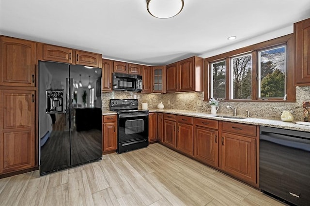 kitchen with a sink, light stone counters, tasteful backsplash, and black appliances