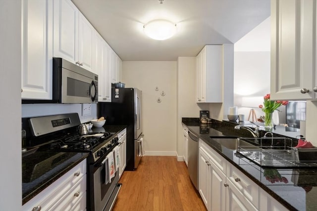 kitchen with appliances with stainless steel finishes, a sink, light wood-type flooring, white cabinetry, and dark stone countertops