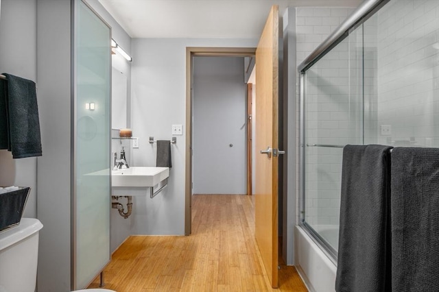 bathroom featuring toilet, wood-type flooring, and bath / shower combo with glass door