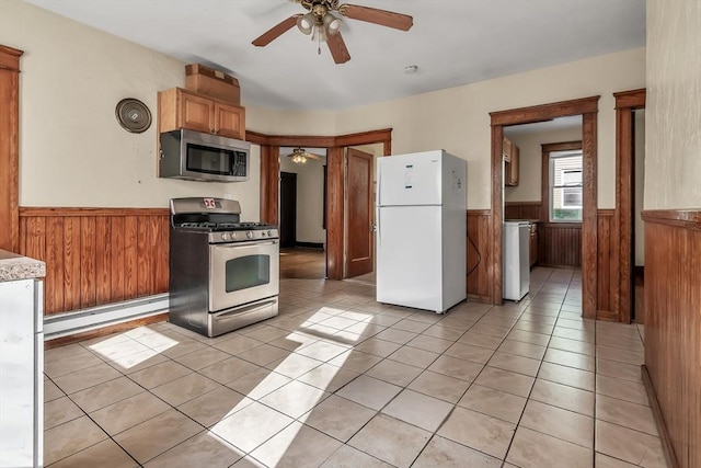 kitchen with a baseboard radiator, appliances with stainless steel finishes, light tile patterned floors, and wooden walls