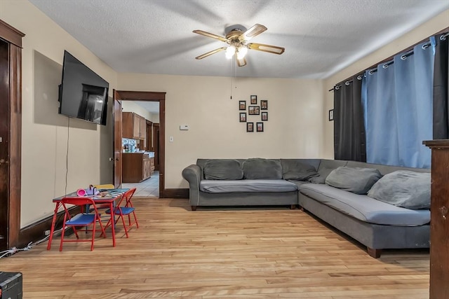 living room with a textured ceiling, ceiling fan, and light wood-type flooring