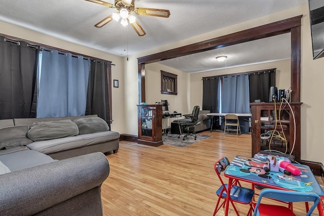 living room featuring ceiling fan, light hardwood / wood-style flooring, and a textured ceiling