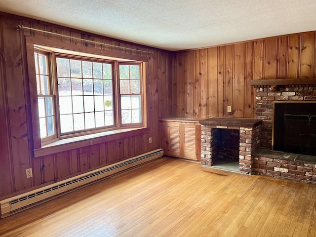 unfurnished living room with light wood-style floors, a baseboard radiator, a textured ceiling, wood walls, and a brick fireplace