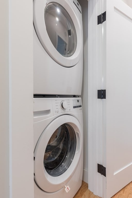 laundry room featuring stacked washing maching and dryer and light hardwood / wood-style flooring