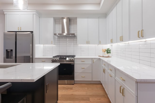 kitchen with white cabinets, wall chimney range hood, light wood-type flooring, tasteful backsplash, and stainless steel appliances