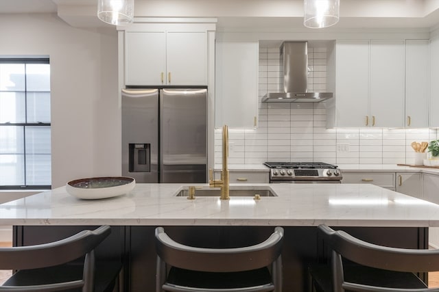 kitchen featuring a kitchen bar, appliances with stainless steel finishes, wall chimney exhaust hood, sink, and white cabinetry