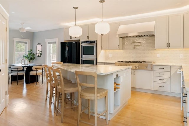 15 Berkeley St, Somerville, MA 02143 - kitchen featuring wall chimney range hood, appliances with stainless steel finishes, tasteful backsplash, and light wood-type flooring