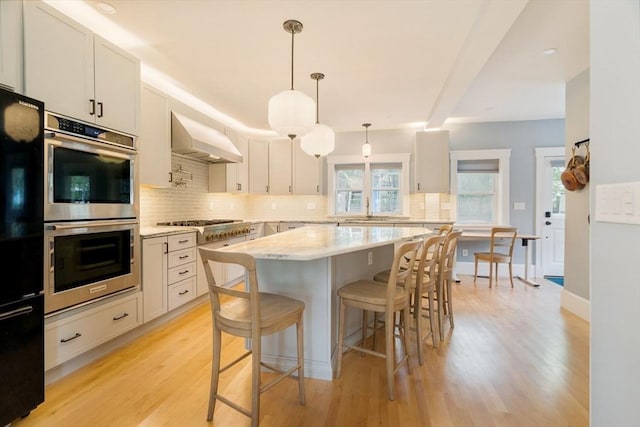 15 Berkeley St, Somerville, MA 02143 - kitchen with appliances with stainless steel finishes, extractor fan, decorative backsplash, a breakfast bar, and light wood-type flooring