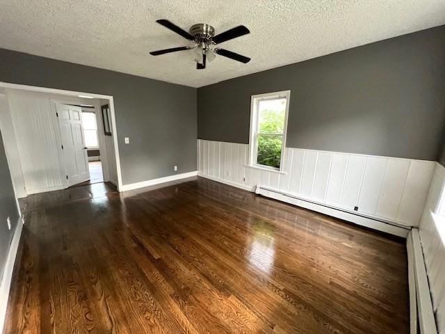 14 Felton St, Fitchburg, MA 01420 - empty room featuring a baseboard radiator, wood finished floors, a textured ceiling, a wainscoted wall, and ceiling fan