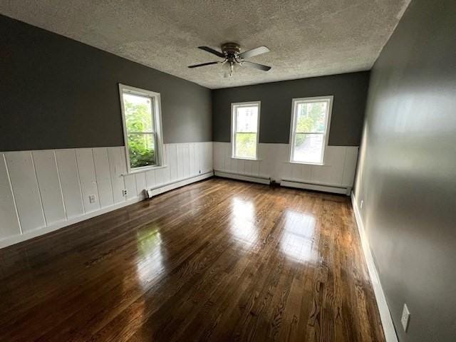14 Felton St, Fitchburg, MA 01420 - empty room featuring a textured ceiling, wood finished floors, wainscoting, a baseboard heating unit, and plenty of natural light