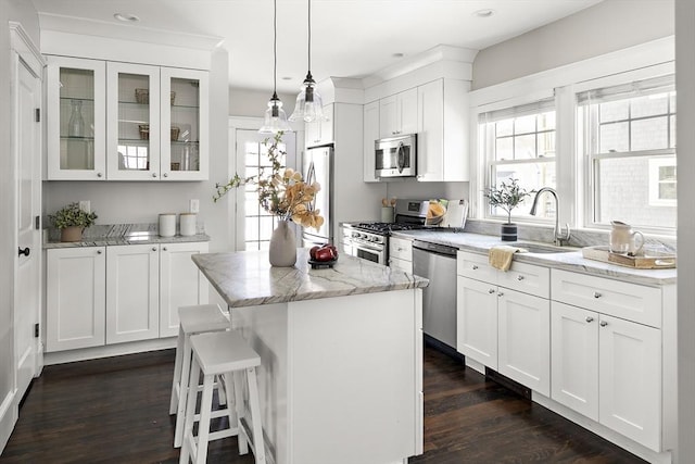 kitchen featuring sink, appliances with stainless steel finishes, a center island, light stone counters, and white cabinets