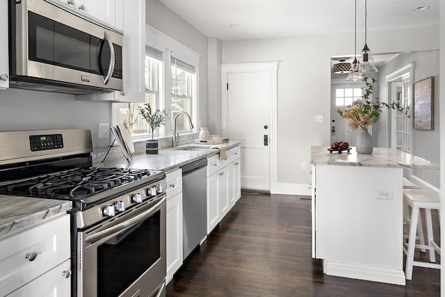 kitchen with sink, white cabinets, hanging light fixtures, stainless steel appliances, and light stone countertops