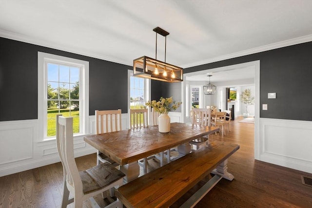 dining space with healthy amount of natural light, a wainscoted wall, a chandelier, ornamental molding, and wood finished floors