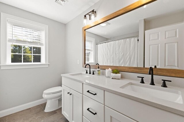 bathroom featuring toilet, baseboards, healthy amount of natural light, and double vanity