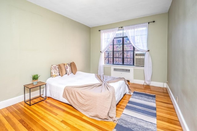 bedroom with wood-type flooring, radiator heating unit, and cooling unit