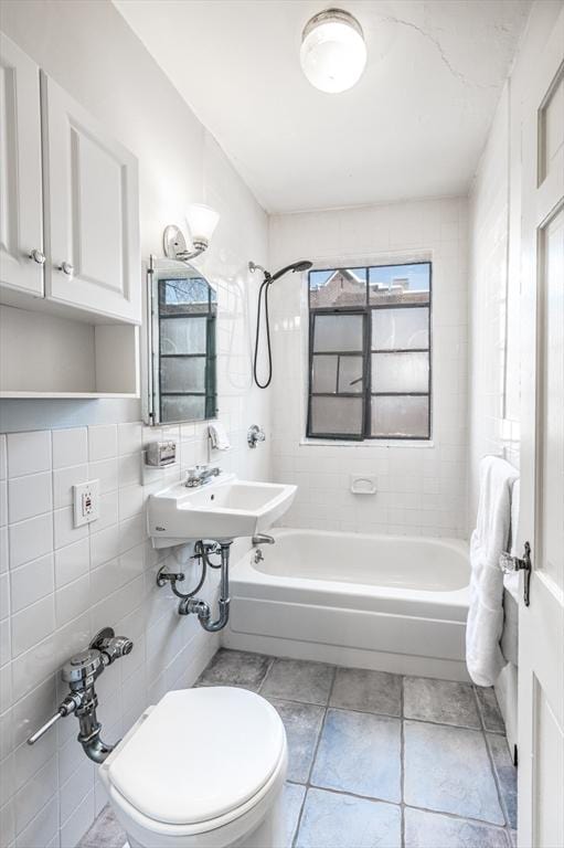 full bathroom with tiled shower / bath combo, sink, toilet, and tile walls