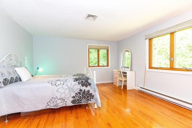 bedroom with visible vents, baseboards, light wood-type flooring, and a baseboard heating unit