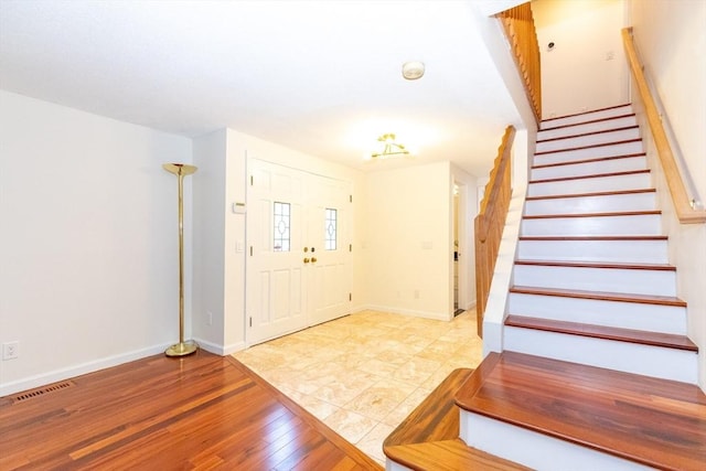 foyer featuring visible vents, baseboards, stairway, and wood finished floors