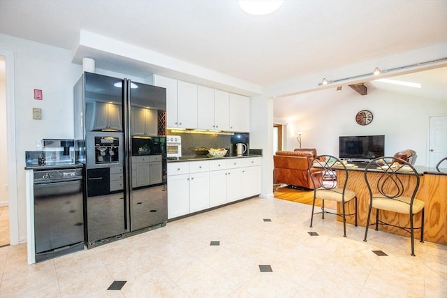kitchen with white cabinets, dark countertops, black fridge, and lofted ceiling with beams