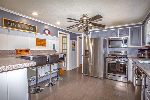 kitchen with crown molding, gray cabinets, a breakfast bar area, appliances with stainless steel finishes, and a textured ceiling