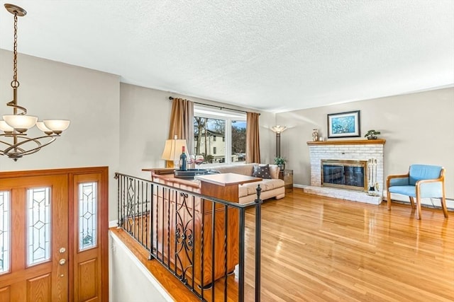 foyer entrance featuring an inviting chandelier, light hardwood / wood-style floors, a textured ceiling, and a brick fireplace