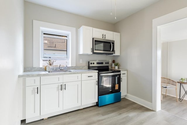 282 Palmer St, New Bedford, MA 02740 - kitchen featuring appliances with stainless steel finishes, a sink, white cabinets, light wood-style flooring, and light countertops