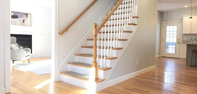 staircase with a fireplace, wood finished floors, and baseboards