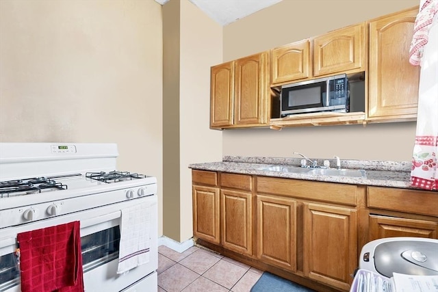 kitchen featuring white range with gas stovetop, light tile patterned floors, light stone counters, and sink