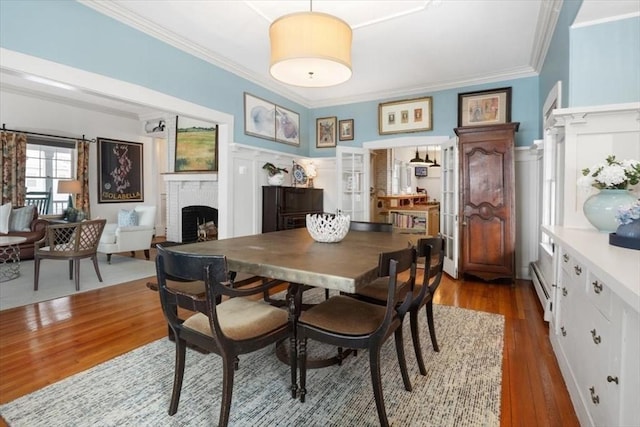 dining area featuring baseboard heating, ornamental molding, wood-type flooring, and a brick fireplace